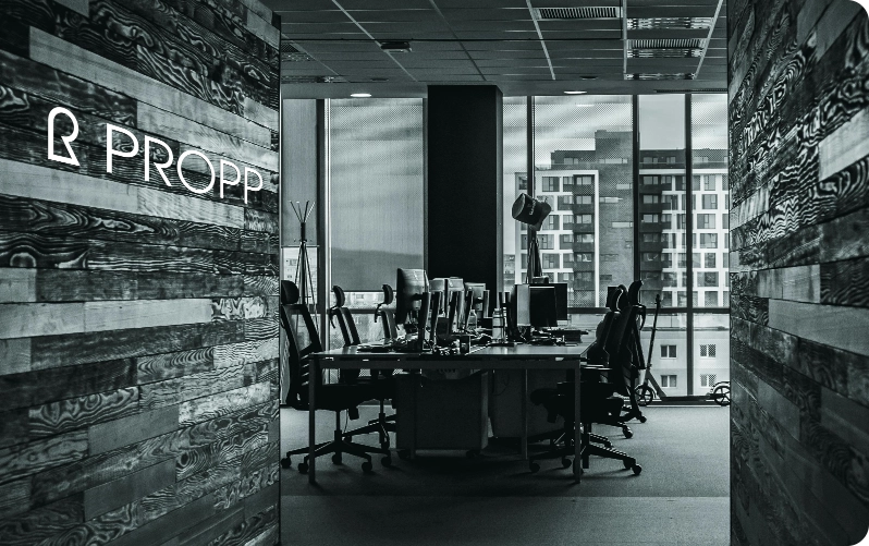 Escritório da Propp com sua logo, uma mesa com várias cadeiras e um monitor para cada